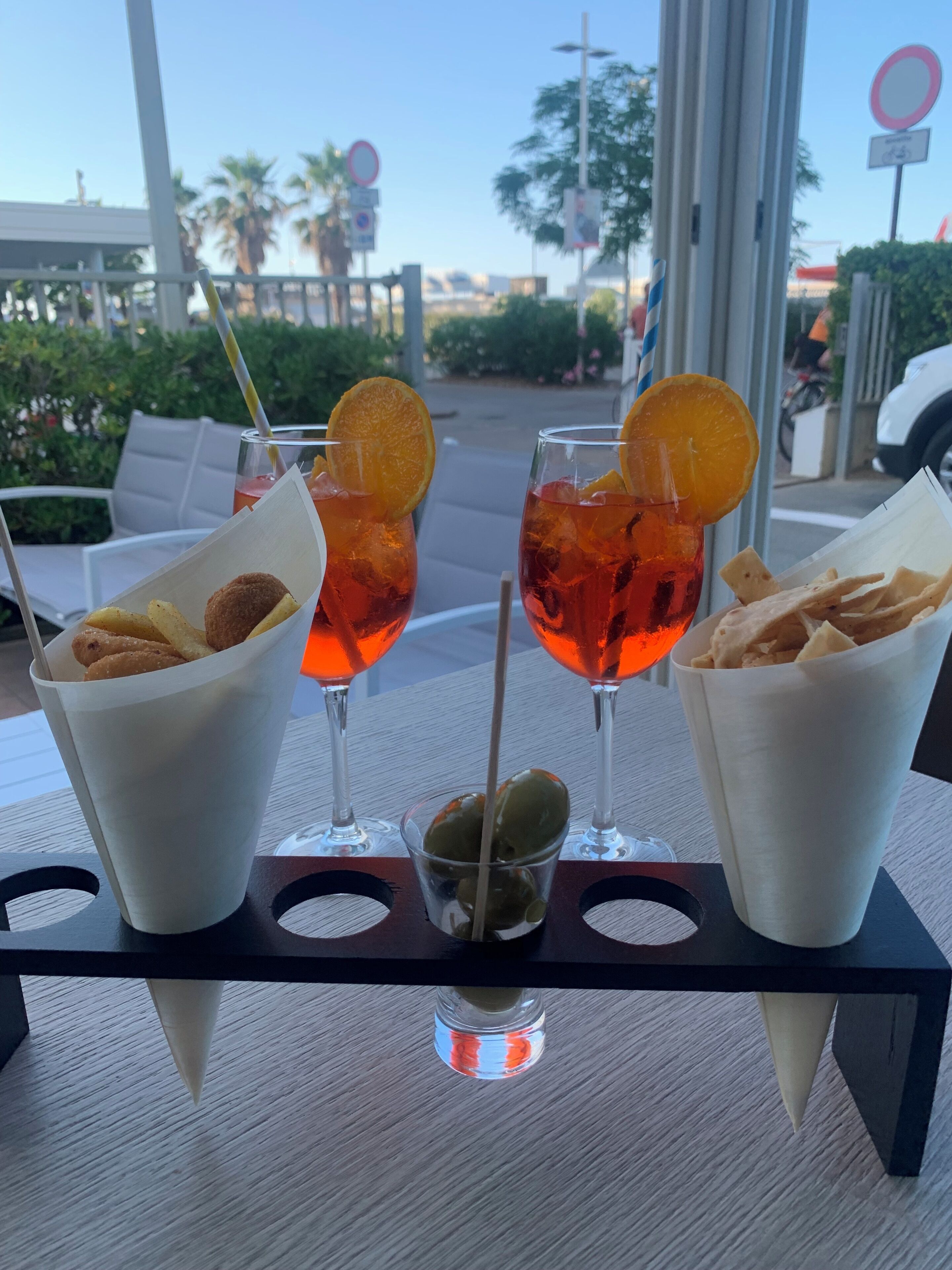A table with three drinks, each garnished with an orange slice, and a small bowl of olives.