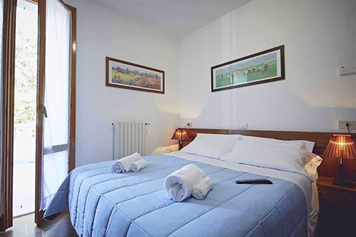 A hotel room with a bed, two paintings on the wall, a window with curtains, and a bedside lamp.