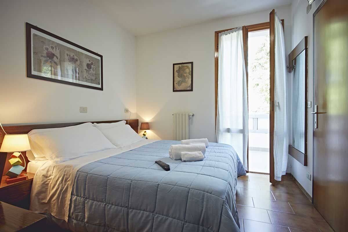 A hotel room with a bed, a nightstand, a lamp, a painting, and a window with curtains.