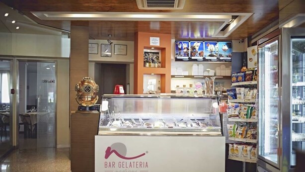 Una heladería con una vitrina de helado, un expositor refrigerado de bocadillos y un área de mesas al fondo.