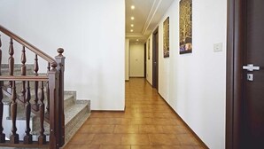 Un pasillo con escaleras de madera, suelo de baldosas y una puerta a la derecha.