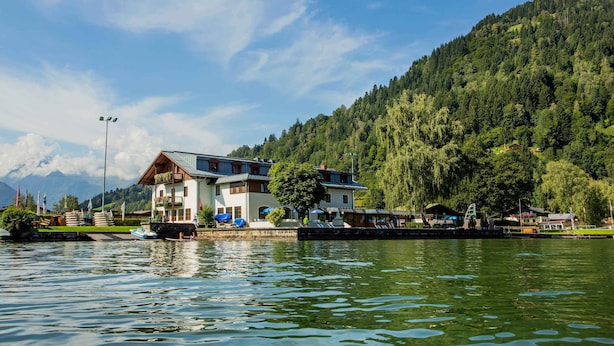 Un edificio sul lago con un balcone, un molo con barche e una montagna boscosa sullo sfondo.