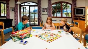 Un gruppo di bambini gioca a giochi da tavolo a un tavolo in una stanza con ampie finestre e vista all'esterno.