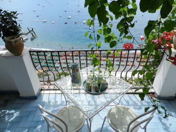 A balcony with a glass table, two chairs, and a potted plant.
