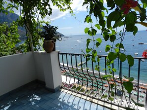 A balcony with a view of the sea, potted plants, and a tiled floor.
