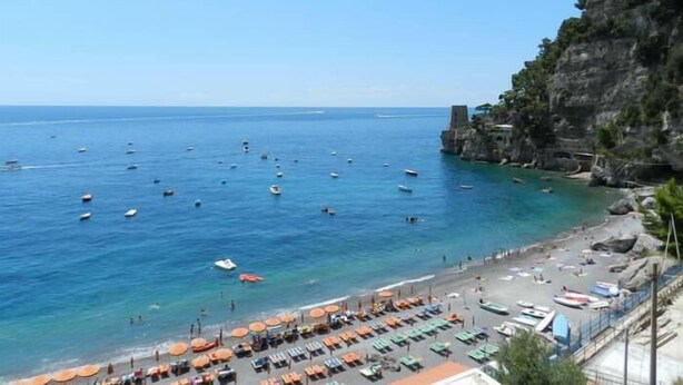 Una playa costera con aguas azules cristalinas, barcos y sombrillas.