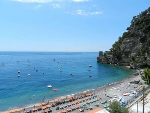 A coastal beach with clear blue waters, boats, and umbrellas.