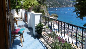 Un balcón con vistas al mar y a las montañas, con plantas en macetas y mobiliario de exterior.