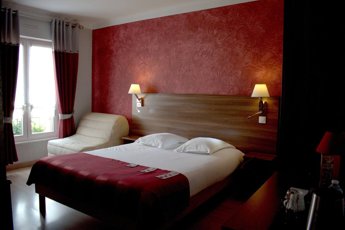 A hotel room with a large bed, a chair, two bedside lamps, and a window with curtains.