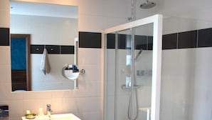 A modern bathroom with a glass-enclosed shower, a wooden vanity with a sink, and a mirror above the vanity. - La Table Alsacienne (Farebersviller)