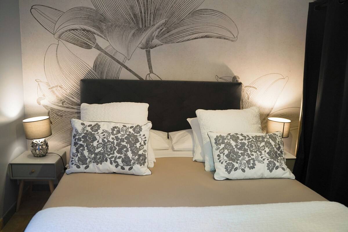 A bed with floral-patterned pillows, a dark headboard, and a wall mural.