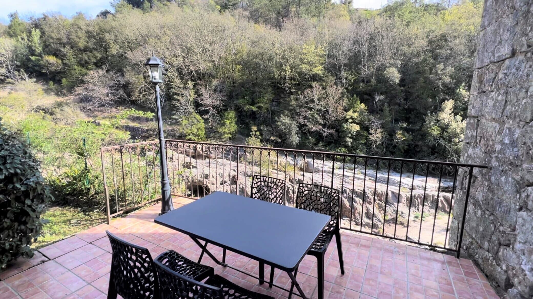 A balcony with a table and chairs, a lamp, and a view of a forested area.