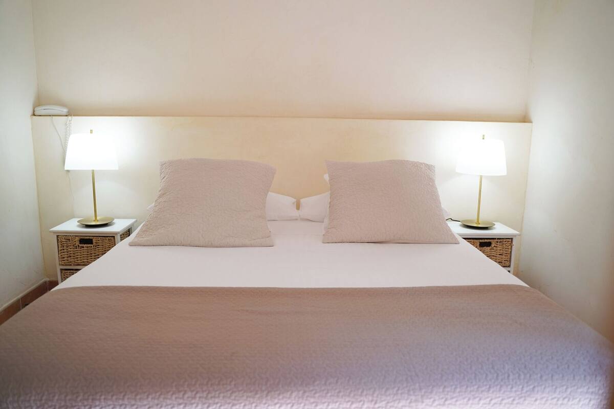 A hotel room with a bed, two bedside lamps, and two pillows.
