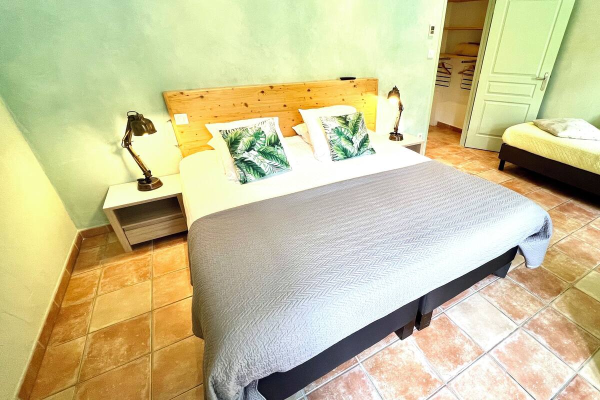 A bedroom with a bed, a nightstand, a lamp, a dresser, and a door.