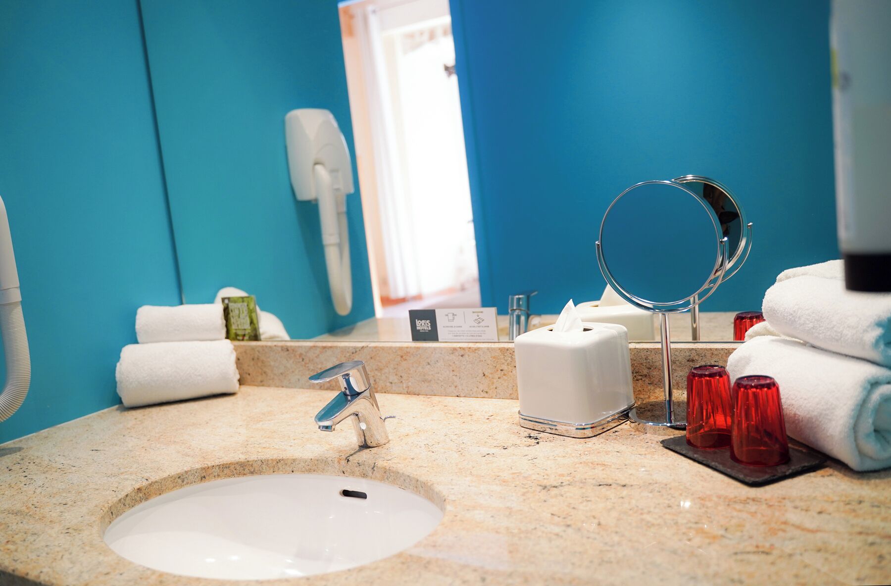 Une salle de bain équipée d’un lavabo, d’un miroir, d’un sèche-cheveux et de serviettes.