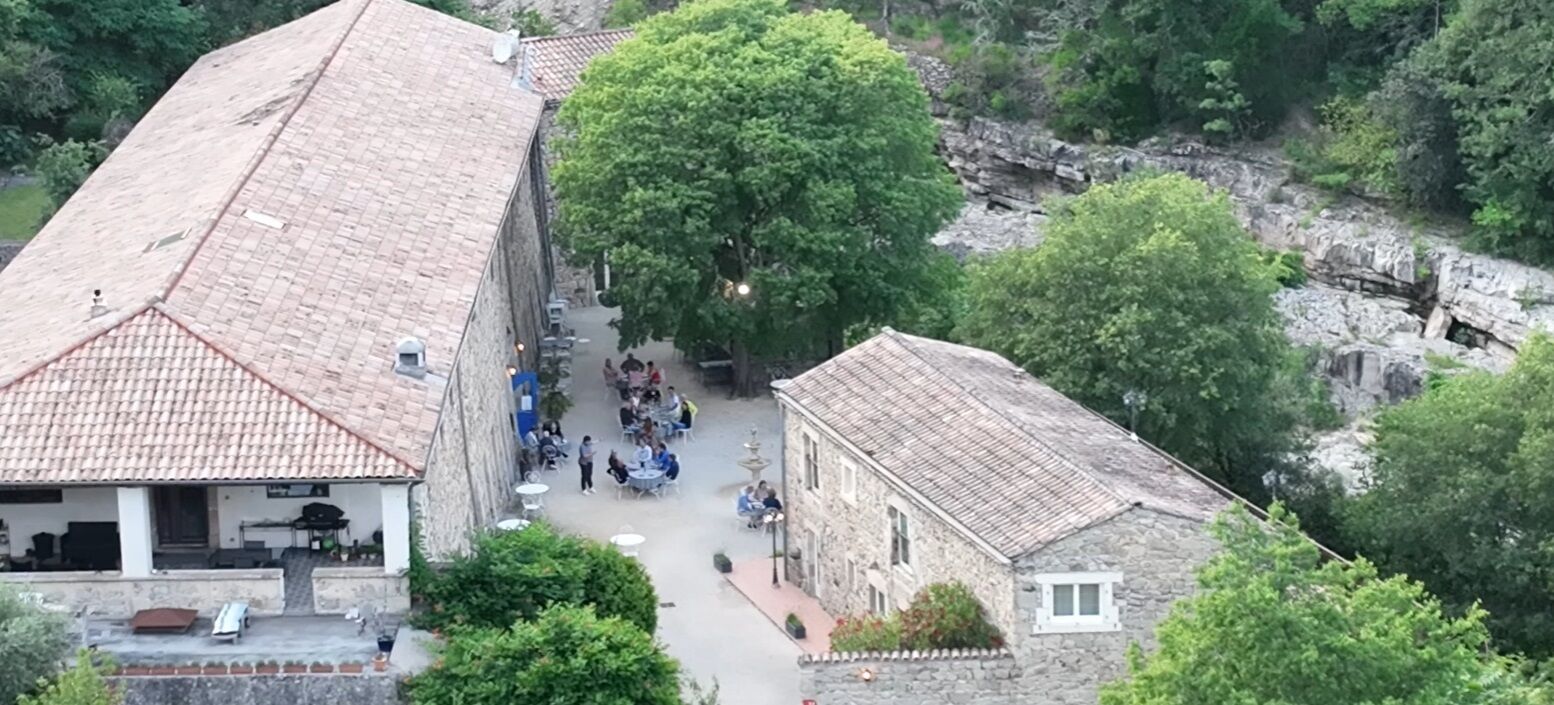 Un patio con edificios de piedra, un árbol grande y un muro de piedra.