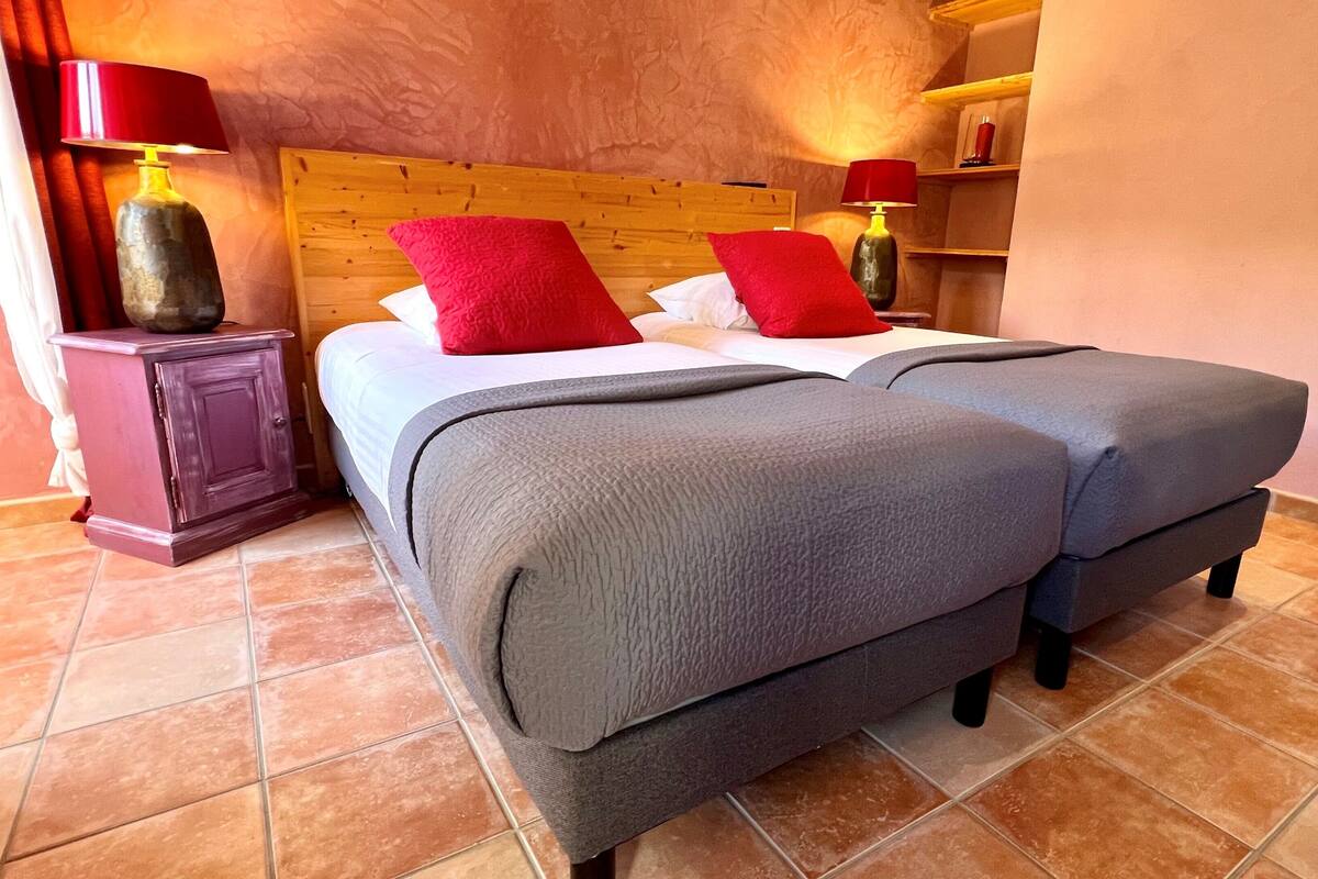 A neatly made bed with a wooden headboard, two red pillows, and a grey blanket.