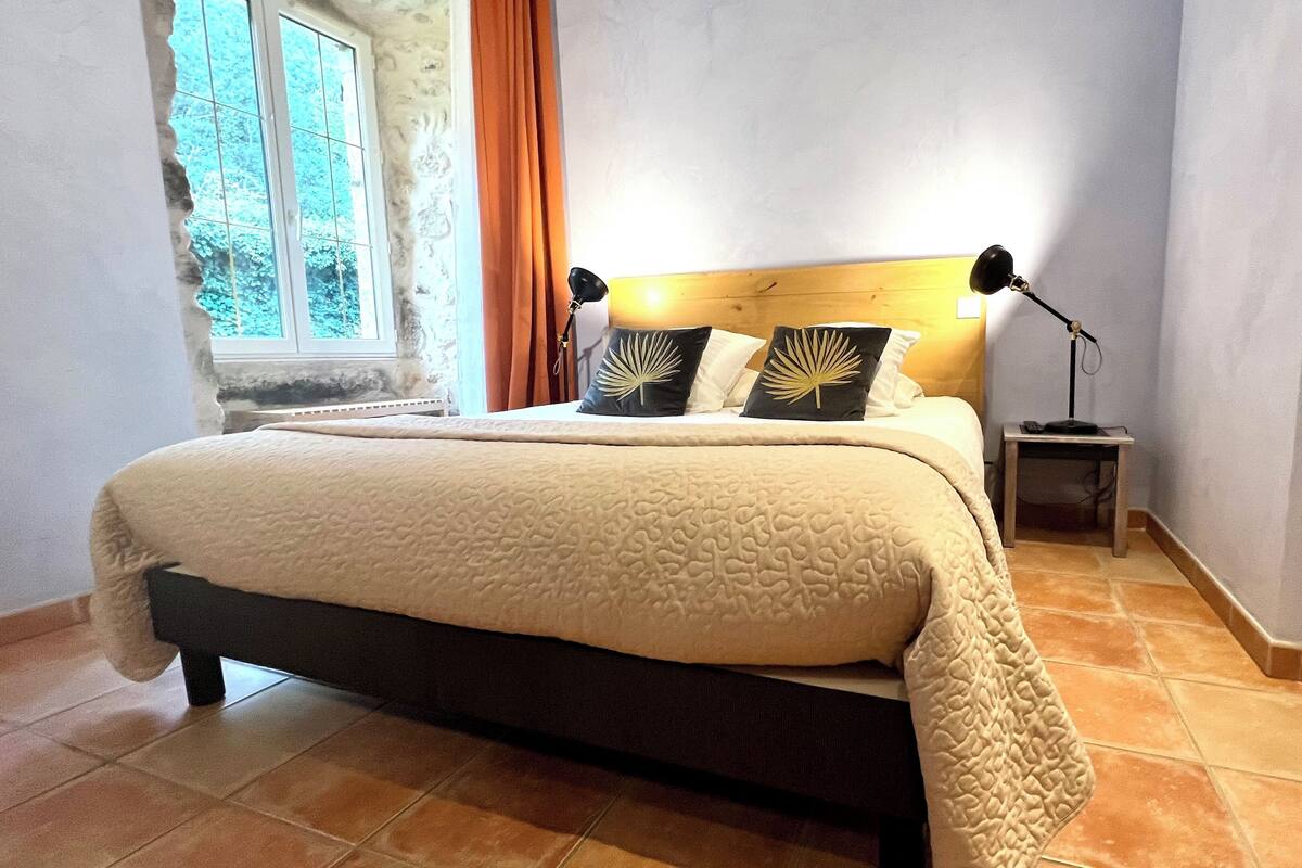 A bedroom with a bed, a nightstand, a lamp, and a window.