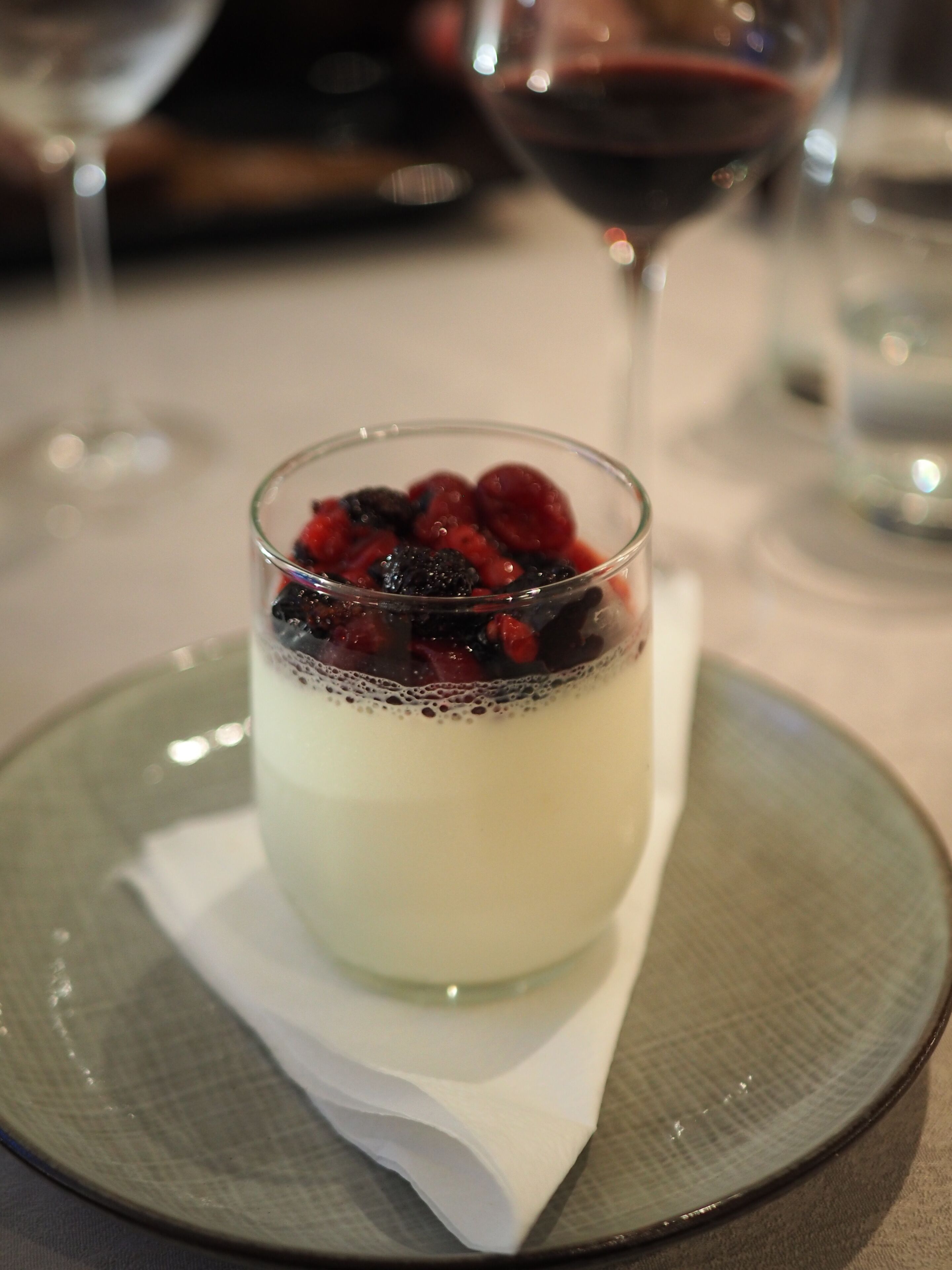 A dessert in a glass cup on a plate with a napkin underneath.