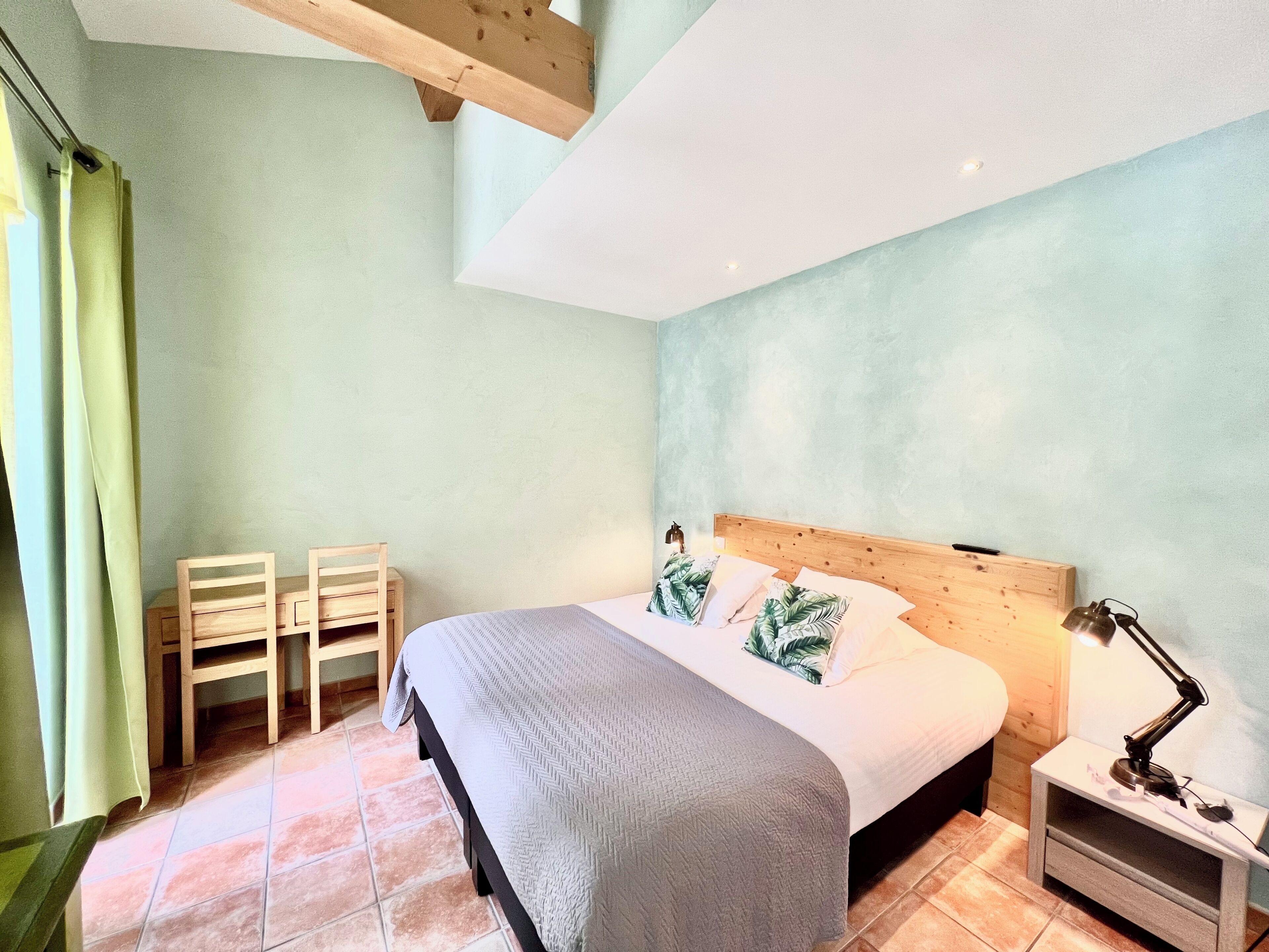A bedroom with a bed, two chairs, a nightstand, and a lamp.
