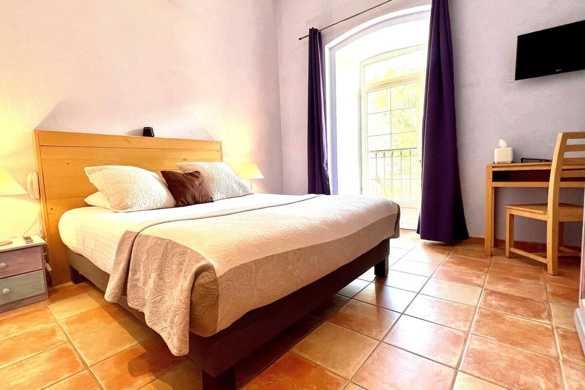 A bedroom with a bed, bedside lamps, a desk with a chair, and a TV on the wall.