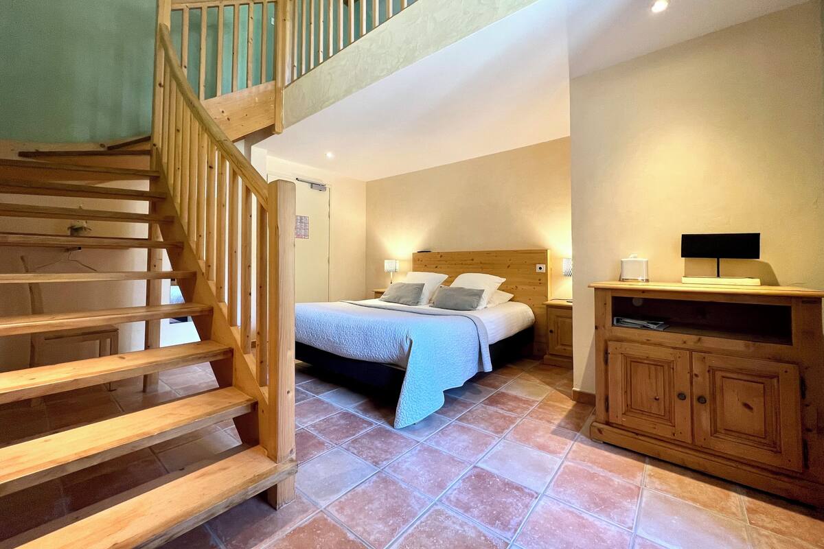 A bedroom with a wooden staircase, a bed with pillows, a nightstand, and a cabinet.