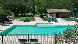 A swimming pool with lounge chairs, a stone building, and a fenced garden area.