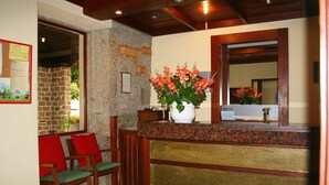 A reception area with a stone wall, wooden chairs, a reception desk with a vase of flowers, and a mirror.