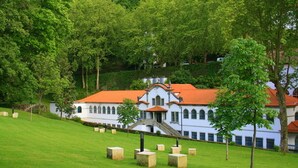A white building with a red roof, surrounded by a grassy area and trees.