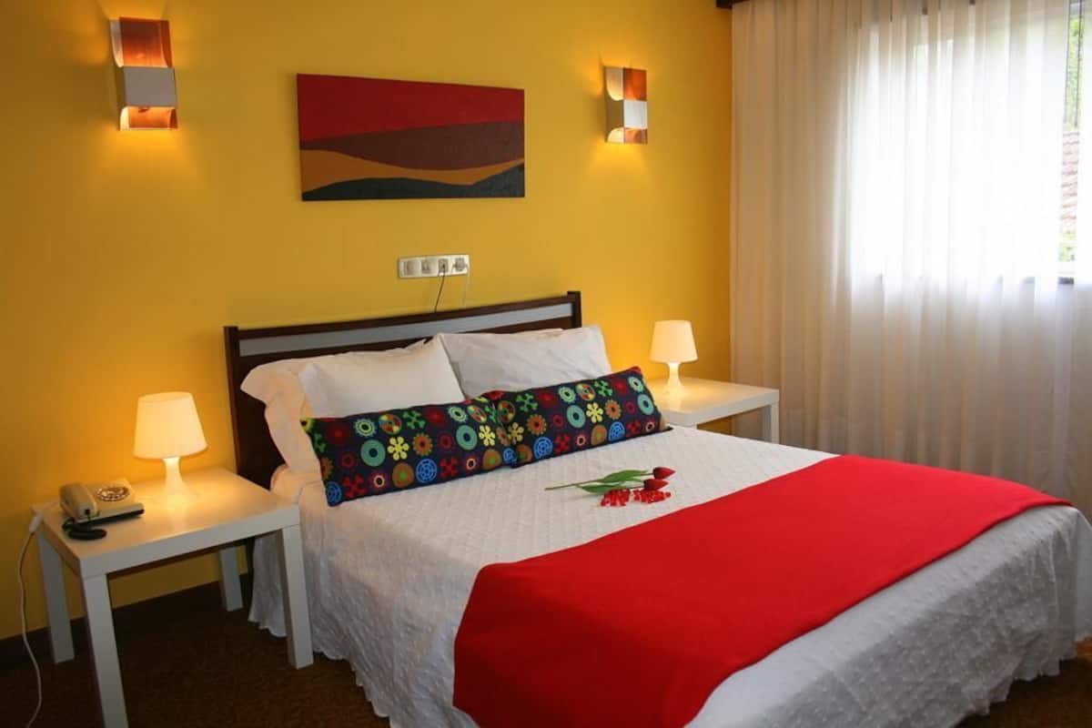 Una habitación de hotel con cama, dos mesitas de noche, lámpara, teléfono y un cuadro en la pared.