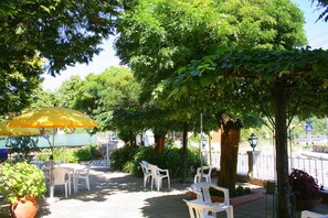 An outdoor patio area with white plastic chairs and a yellow umbrella, surrounded by lush greenery and trees. - Corredoura Garden Alojamento (Amares)