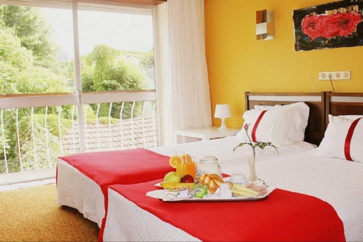 Habitación de hotel con una cama grande, un balcón con barandilla blanca y vistas a la vegetación.