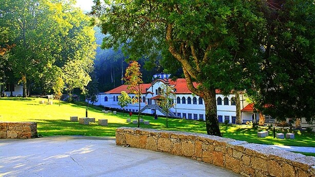 A building with a red roof, surrounded by a stone wall and trees.