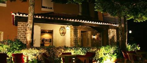 An outdoor dining area with stone walls, potted plants, and red chairs.