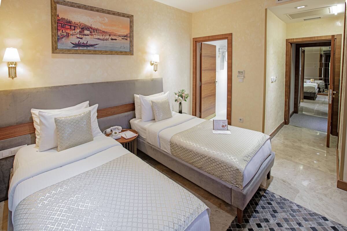 Ein Hotelzimmer mit zwei Betten, einem Nachttisch, einer Lampe, einem Bild und einem durch eine offene Tür einsehbaren Badezimmer.