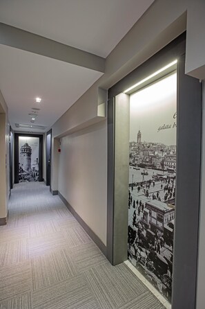 A hallway with a patterned carpet, a wall-mounted light, and a large poster of a cityscape. - Nowy Efendi Hotel - Special Class (Istanbul)