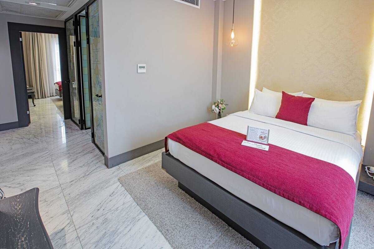 Ein Hotelzimmer mit einem großen Bett, einem kleinen Tisch, einem Spiegel und einer Tür zu einem weiteren Raum.