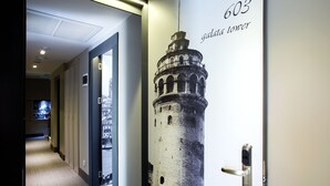 Un pasillo con un cartel del Galata Tower, una puerta con picaporte moderno y suelo alfombrado.