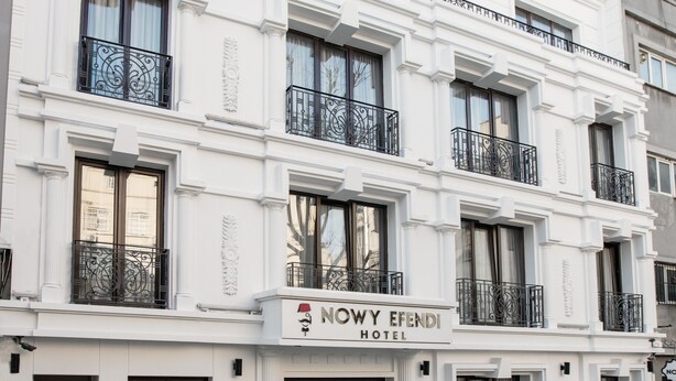 Un edificio blanco con balcones, un letrero que dice "NOWY EFENDI HOTEL" y una calle empedrada.