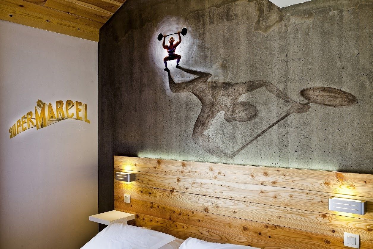 A hotel room with a concrete wall mural, wooden headboard, and a bed with white linens.