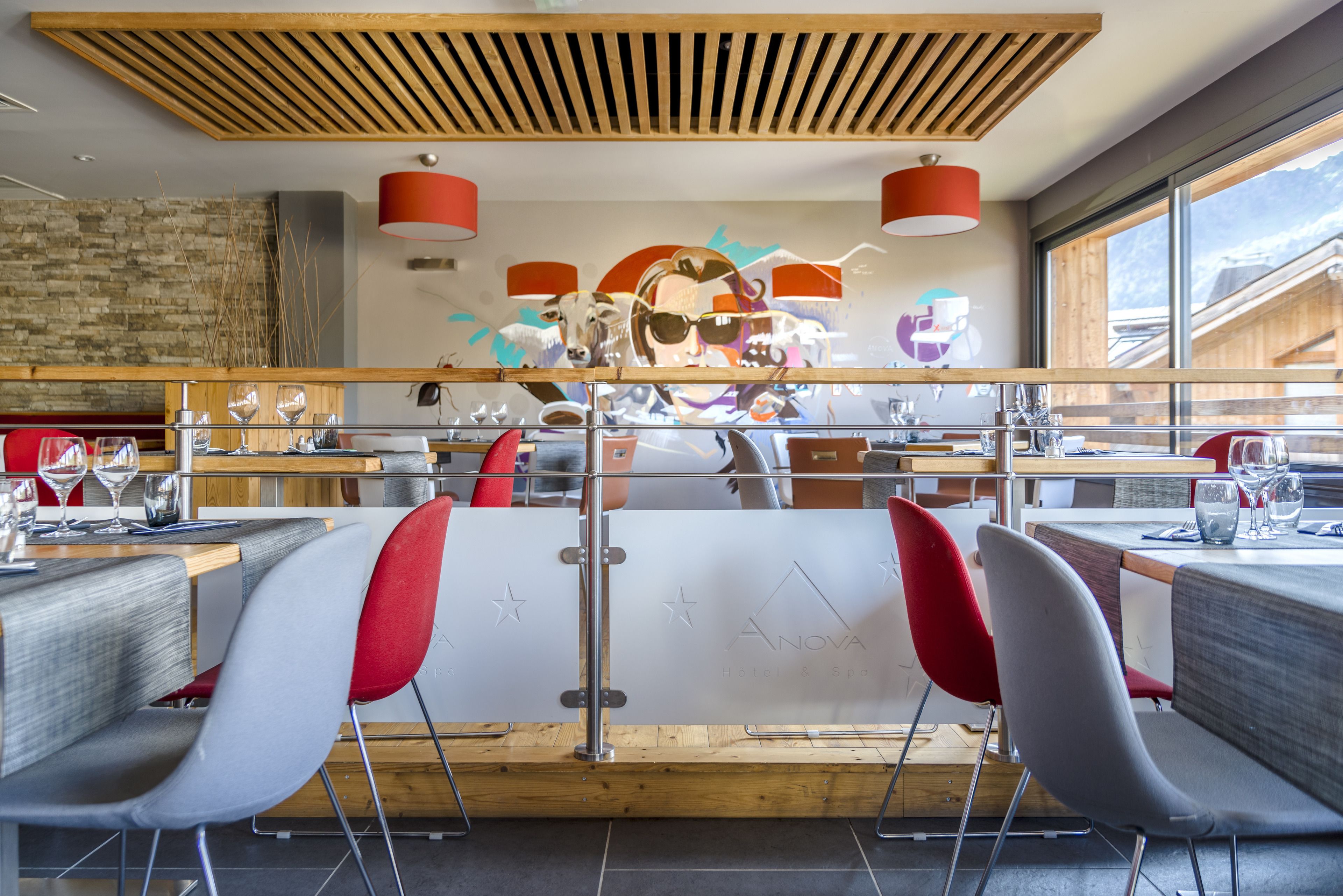 A modern restaurant with a wooden ceiling, red and grey chairs, and a mural on the wall.