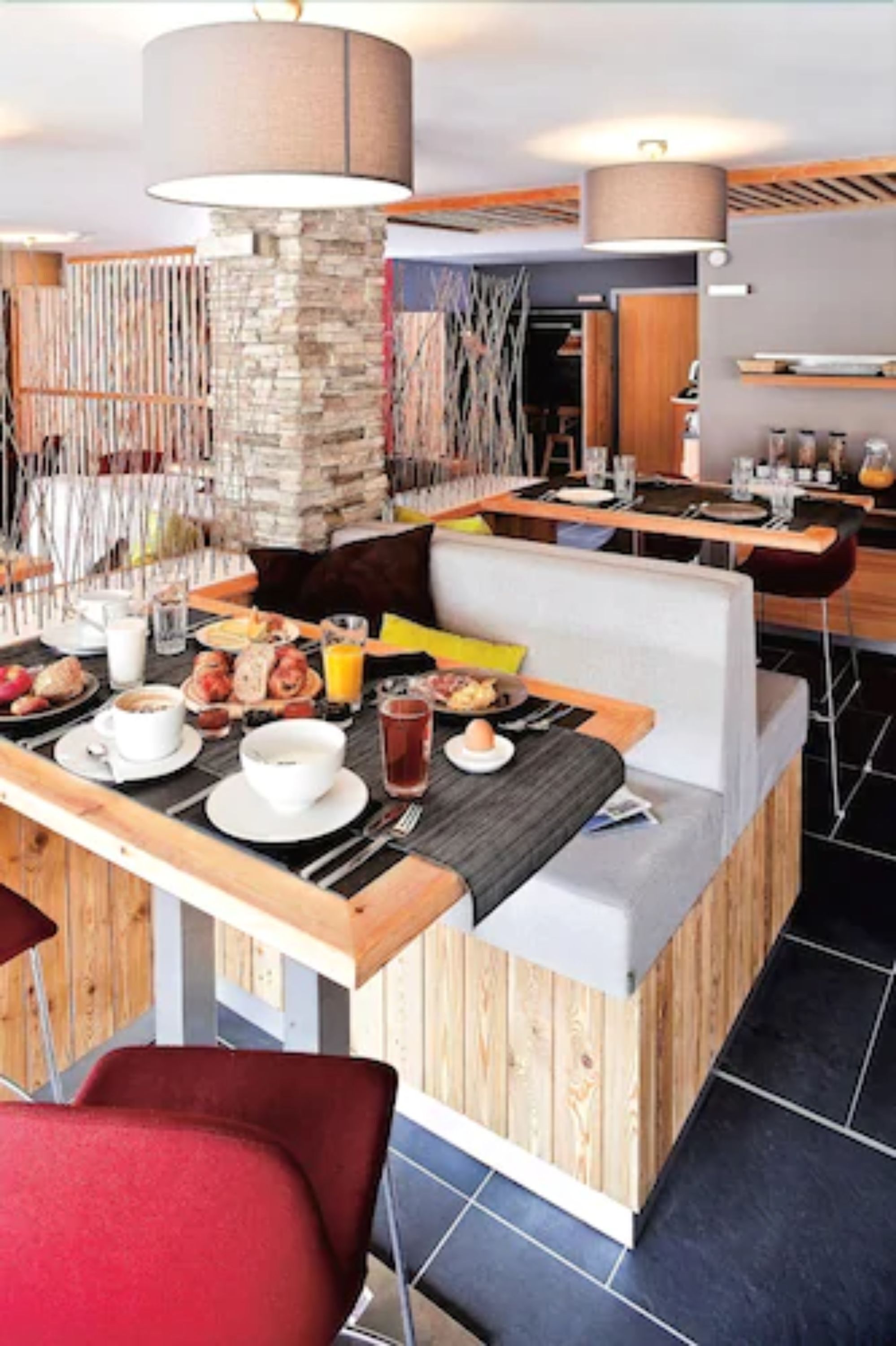 A breakfast setup with a wooden table, a stone pillar, and a modern seating area.