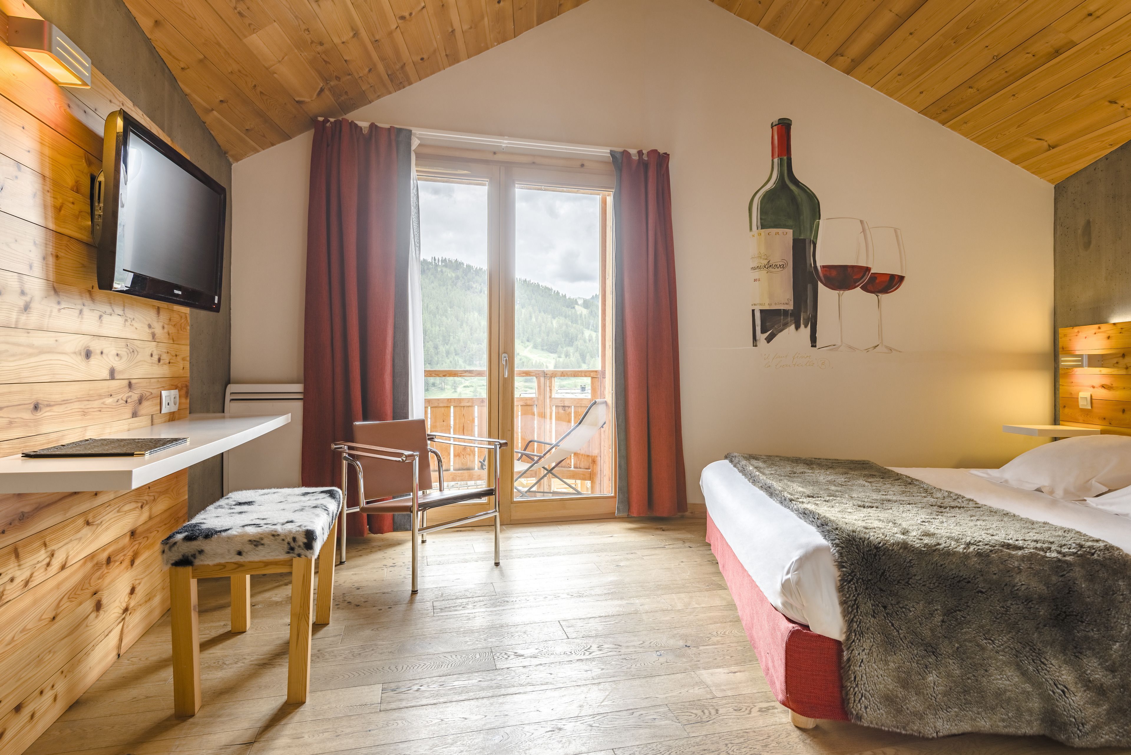 Een gezellige kamer met een bed, een bureau met een stoel, een televisie en uitzicht op de omgeving via een glazen deur.