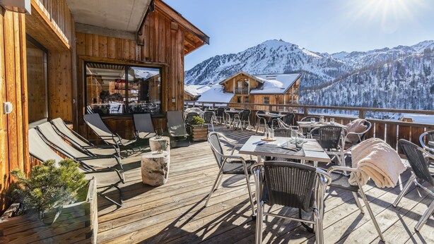 Um deck de madeira com área de estar externa, bar e vista para montanhas cobertas de neve.
