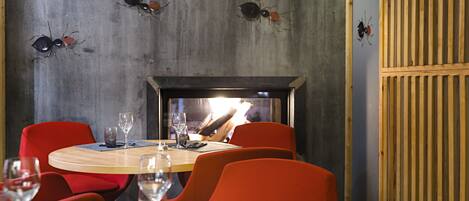A restaurant with round tables, red chairs, and a fireplace.