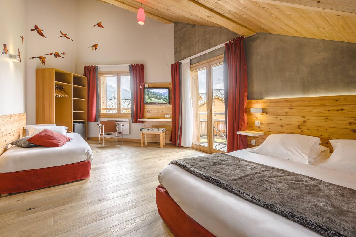 A bedroom with two beds, wooden flooring, a desk, and a chair.