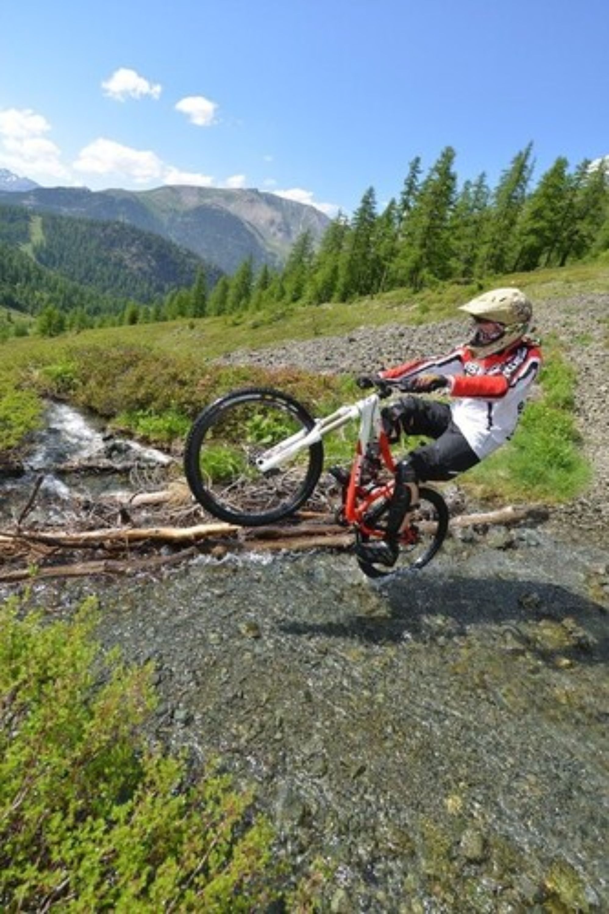 A mountain biker navigating a rocky terrain with a clear view of distant mountains and a forested area.