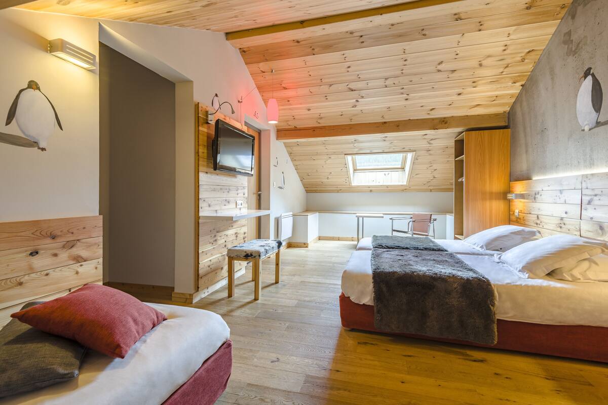 A cozy room with wooden floors, a bed with a fluffy blanket, a small table, and a TV mounted on the wall.