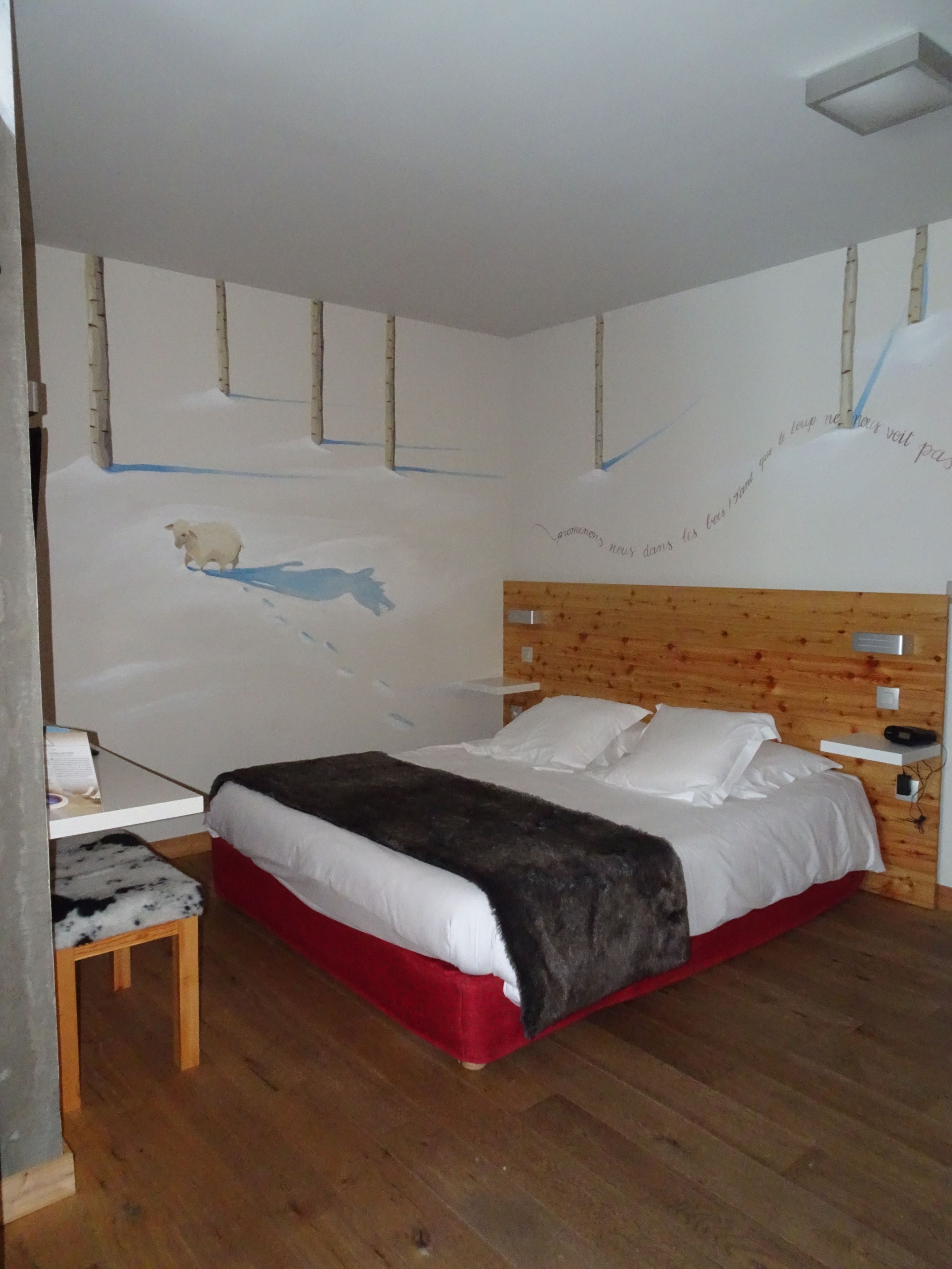 Un dormitorio con cabecera de madera, una cama con ropa de cama blanca, una mesita de noche pequeña y una silla.