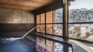 Uma área de spa com hidromassagem, grandes janelas e vista para montanhas nevadas.